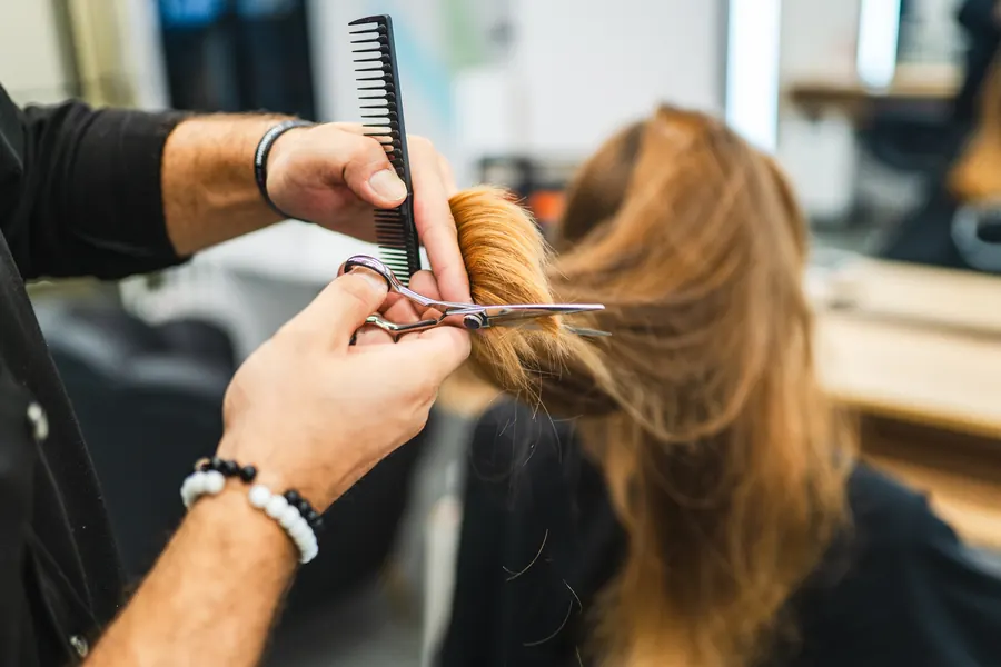 Stylist trimming long hair with scissors and a comb
